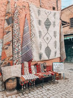 an outdoor seating area with various rugs and pillows on display in front of a brick building