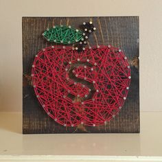 a string art apple with a dollar sign on it's side, sitting on a shelf