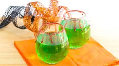 three glasses with green liquid sitting on top of a table next to ribboned ribbons