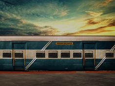 a blue and white train parked next to a loading platform at sunset with the sky in the background