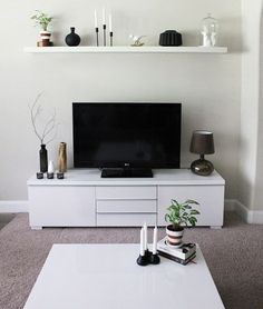 a living room with a white coffee table and shelves on the wall above it is a flat screen tv