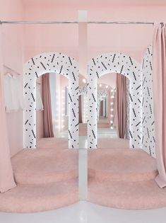 a pink and white room with curtains on the walls, two round mirrors in the middle