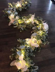 some white flowers and green leaves on a wooden floor with lights in the middle of it