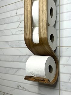 three rolls of toilet paper are hanging on a wooden holder in a white tiled bathroom