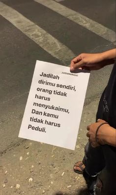 a person sitting on the ground holding up a sign that says, jadifah dimu sendi, orange tidak