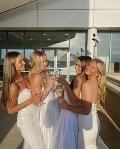 three beautiful women standing next to each other holding wine glasses in front of a building