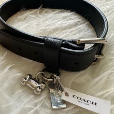 a coach belt with two charms attached to it on top of a white furnishing