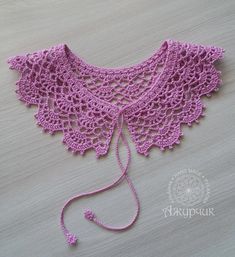 a pink crocheted shawl on top of a wooden table next to a string