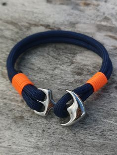 an orange and blue rope bracelet with two silver anchor clasps on top of it