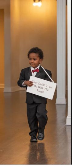 a little boy in a suit and bow tie holding a sign