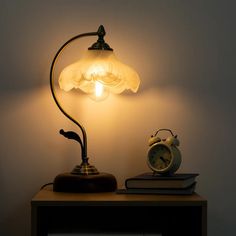 a lamp that is on top of a table next to a book and an alarm clock