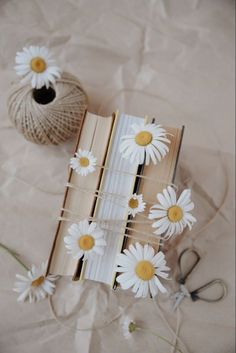 an open book with daisies on it next to some scissors and twine spools