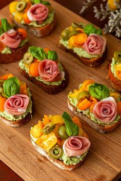 many small sandwiches are arranged on a cutting board with vegetables and meats in the middle