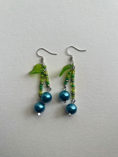 the earrings are made with green beads and leaves on them, while blue pearls hang from silver earwires