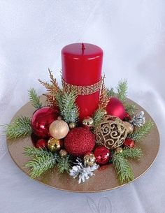 a red candle sitting on top of a gold plate filled with ornaments and greenery