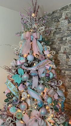 a pink and blue christmas tree decorated with bows, ornaments and ribbons is in front of a brick wall