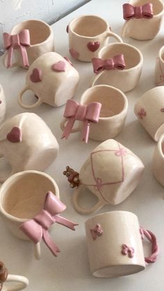 many cups with bows and hearts on them are sitting on a white surface, surrounded by smaller ones