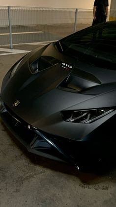 a black sports car parked in a parking lot next to a person standing near it