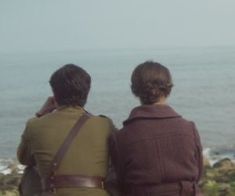 two people sitting on rocks looking out at the ocean