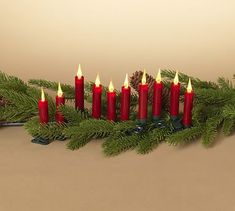 a group of red candles sitting on top of a green christmas tree next to pine cones