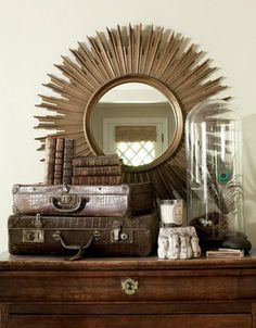 a dresser topped with lots of luggage and a sunburst shaped mirror above it