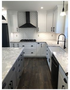 a large kitchen with white cabinets and marble counter tops, an oven hood over the range