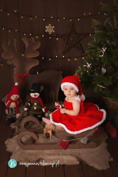 a baby dressed up as santa claus sitting in front of a christmas tree and toys