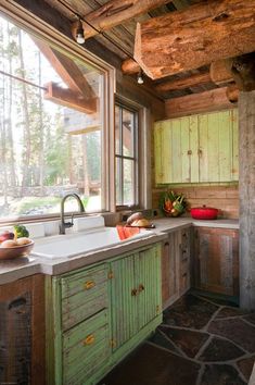 a kitchen with green cabinets and stone flooring in front of a window that looks out onto the woods