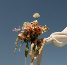 a woman holding a bouquet of flowers in her hand under a blue sky with white drapes