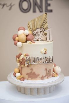 a three tiered cake decorated with balloons and an animal on top is sitting on a table