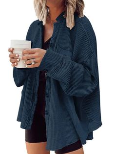 a woman holding a coffee cup and wearing a blue cardigan sweater with black shorts