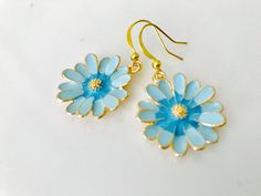 Beautiful Blue and gold enamel daisy earrings. Freshen up your spring and summer wardrobe with these eye-catching blue daisy dangles. The pedala are light blue with a slightly darker blue and gold. Trimmed in gold, they dangle from gold French hooks. Comes with a secured rubberized backing. they will arrive beautifully packaged and ready for gifting. Blue Dangle Earrings For Spring, Light Blue Flower Jewelry For Spring, Blue Flower Shaped Earrings For Summer, Blue Flower-shaped Summer Earrings, Blue Flower-shaped Spring Jewelry, Light Blue Jewelry For Spring Gift, Blue Flower Charm Earrings For Spring, Blue Dangle Flower Earrings For Spring, Blue Earrings With Flower Charm For Spring