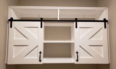 a white cabinet with sliding doors and black hardware on the bottom shelf, in a room