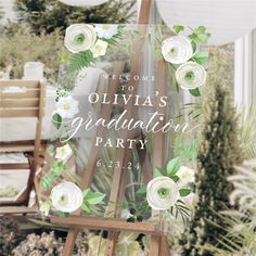 an easel with flowers and greenery on it is in front of a sign that says welcome to oliva's graduation party