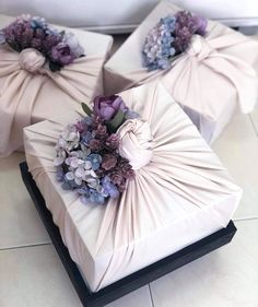 three wrapped gift boxes with purple flowers on the top and one tied up to the side