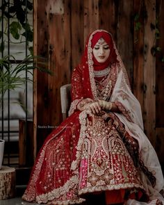 a woman in a red and white bridal outfit sits on a chair with her hands clasped to her knees