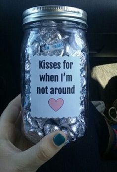 a person holding up a jar full of candy with the words kisses for when i'm not around