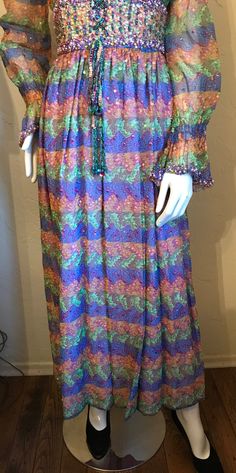 "This is a gorgeous vintage 1970's bohemian dress. It is a colorful peacock feather print polyester chiffon accented with sequins and beading in a peasant style dress. The bodice is smocked and has a scoop neck wide beaded corset style waist with beaded tie bow and sheer sleeves with smocked ruffle cuffs, The skirt is fully gathered and is lined. It has a full nylon zipper up the back. It is in good condition...there may be a few loose sequins, and smocking at cuffs is a little stretched. Priced Multicolor Sequined Maxi Dress, Spring Multicolor Sequined Maxi Dress, Bohemian Beaded Dresses For Spring, Bohemian Long Sleeve Beaded Dress, Bohemian Floor-length Sequined Maxi Dress, Peacock Feather Print, Beaded Corset, Beaded Tie, Peasant Style Dress