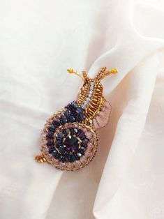 a close up of a napkin on a white table cloth with a gold and black beaded brooch