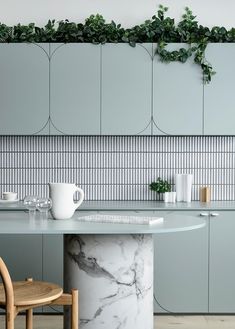 a kitchen with marble counter tops and green plants on the wall above it, along with two wooden chairs