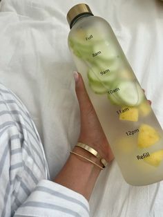 a woman is holding a bottle with lemon slices in it and her hand on the bed