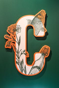 the letter c is decorated with flowers and fish on it's back side in orange and white