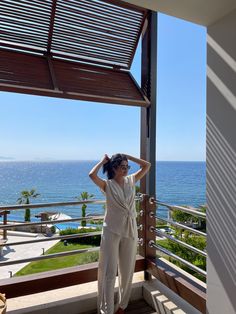 a woman standing on top of a balcony next to the ocean with her hand on her head