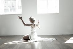 a woman in a white dress sitting on the floor with her arms up and legs crossed