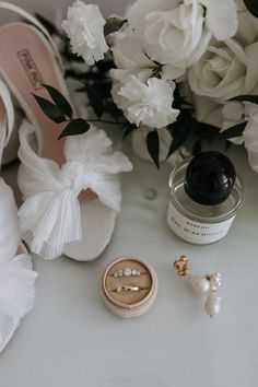 two wedding rings sitting on top of a white table next to flowers and other accessories