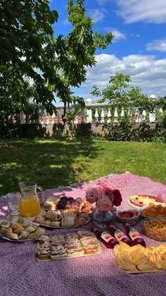 a table with food and drinks on it in the shade of a tree, under a blue sky