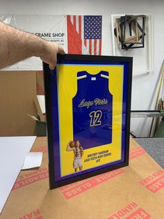 a person holding up a framed basketball jersey in front of a box with the number 12 on it