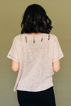 the back of a woman's sweater with crochet on it and black pants