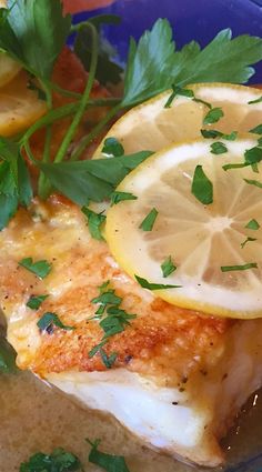 a blue plate topped with fish covered in lemons and parsley