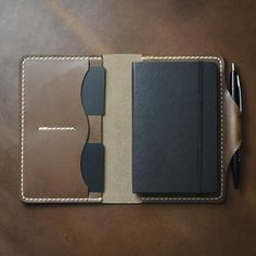 a notebook and pen sitting on top of a brown leather cover covered in stitching